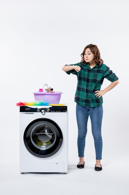 Vista frontal de uma jovem mulher com máquina de lavar roupa na parede branca