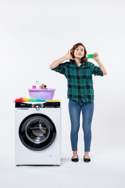 Vista frontal de uma jovem mulher com máquina de lavar segurando um cartão do banco verde na parede branca