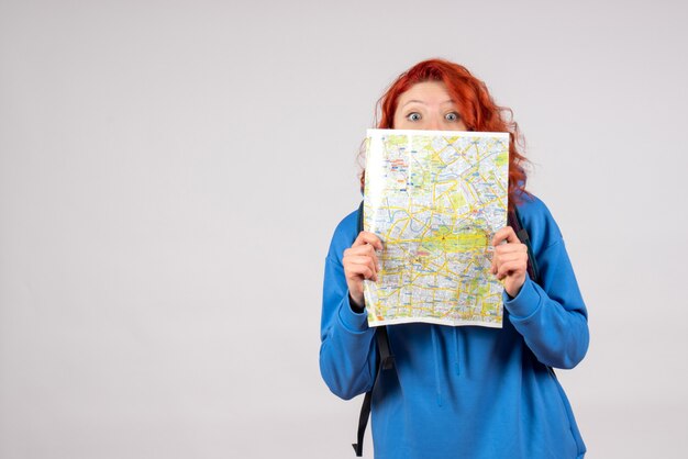 Vista frontal de uma jovem mulher com mochila e mapa na parede branca