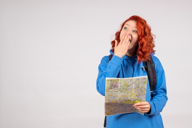 Vista frontal de uma jovem mulher com mochila e mapa na parede branca