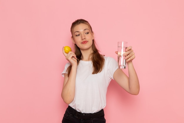 Vista frontal de uma jovem mulher com uma camiseta branca segurando um limão fresco e um copo de água