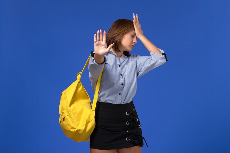 Foto grátis vista frontal de uma jovem mulher de camisa azul com saia preta e mochila amarela na parede azul-clara