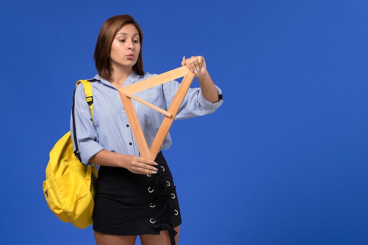 Foto grátis vista frontal de uma jovem mulher de camisa azul segurando um triângulo de madeira na parede azul