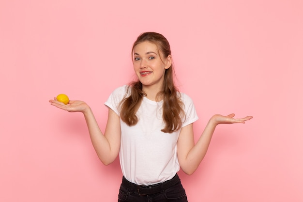 Vista frontal de uma jovem mulher de camiseta branca segurando limão fresco na parede rosa