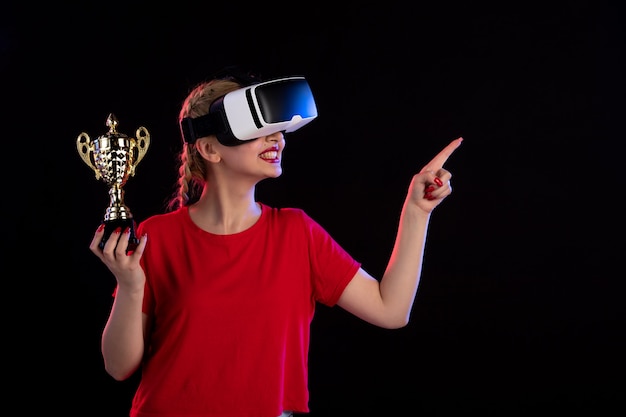 Vista frontal de uma jovem mulher jogando vr e ganhando a taça no visual do jogo escuro d