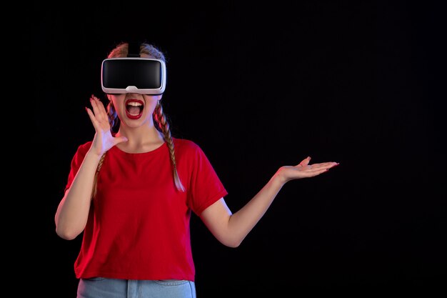 Vista frontal de uma jovem mulher jogando vr na parede escura