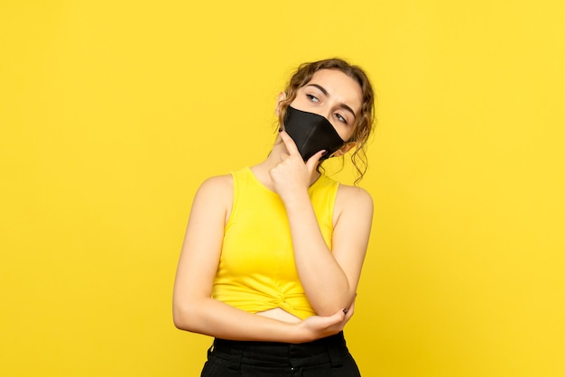 Vista frontal de uma jovem pensando em máscara preta na parede amarela