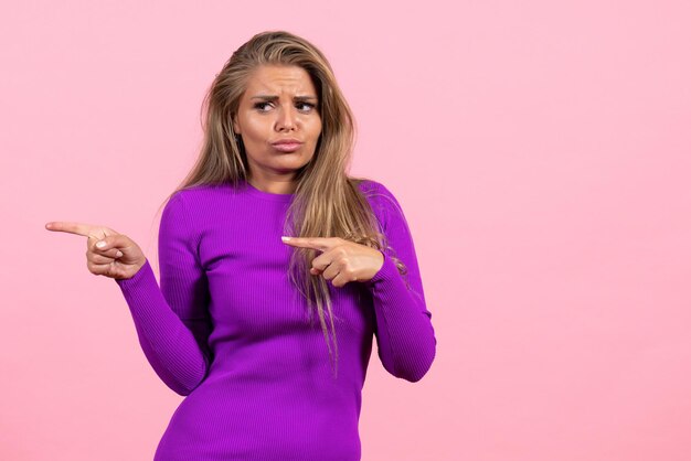 Vista frontal de uma jovem posando com um lindo vestido roxo na parede rosa claro