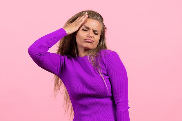 Vista frontal de uma jovem posando com um lindo vestido roxo na parede rosa