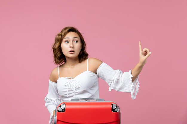 Vista frontal de uma jovem posando com uma sacola de férias vermelha na parede rosa