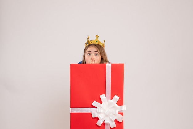 Vista frontal de uma jovem se escondendo dentro de uma caixa de presente na parede branca