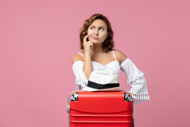 Vista frontal de uma jovem se preparando para as férias com uma bolsa vermelha posando na parede rosa