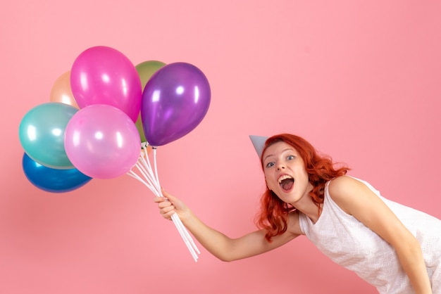 Vista frontal de uma jovem segurando balões coloridos na parede rosa