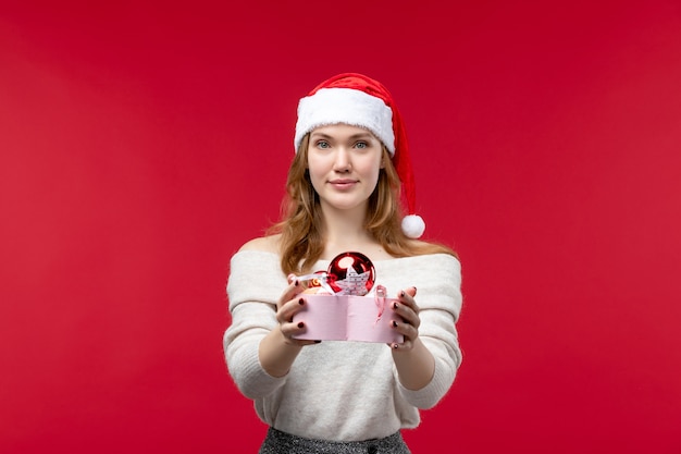 Foto grátis vista frontal de uma jovem segurando brinquedos de natal no chão vermelho. natal, feriado, vermelho
