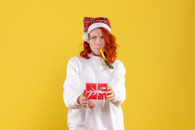 Vista frontal de uma jovem segurando o pequeno presente de Natal na parede amarela