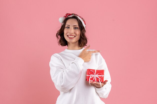 Vista frontal de uma jovem segurando o pequeno presente de Natal na parede rosa