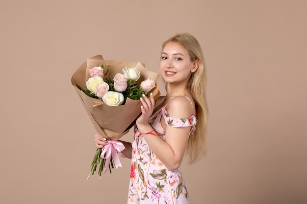 Vista frontal de uma jovem segurando um buquê de lindas rosas na parede marrom