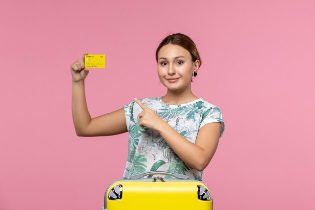 Vista frontal de uma jovem segurando um cartão amarelo na parede rosa