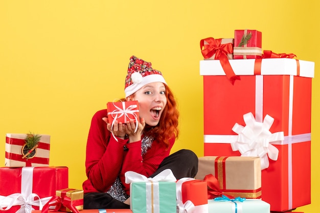 Vista frontal de uma jovem sentada ao redor do Natal apresenta-se na parede amarela