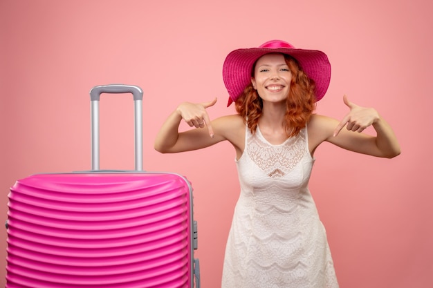 Vista frontal de uma jovem turista com chapéu rosa e bolsa na parede rosa