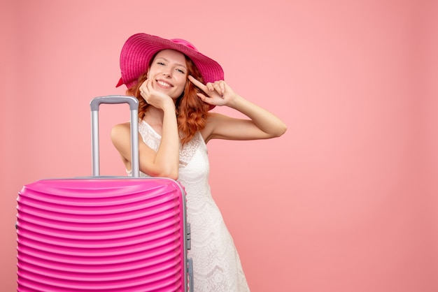 Vista frontal de uma jovem turista com chapéu rosa e bolsa na parede rosa