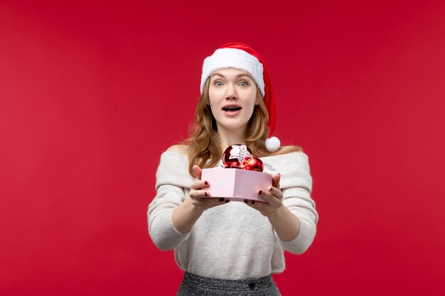 Vista frontal de uma linda mulher segurando brinquedos de natal no vermelho