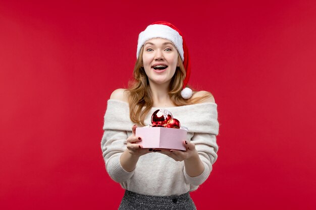 Vista frontal de uma linda mulher segurando brinquedos de natal no vermelho