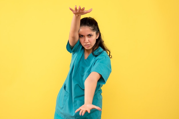 Vista frontal de uma médica bonita mostrando o tamanho com as mãos na parede amarela