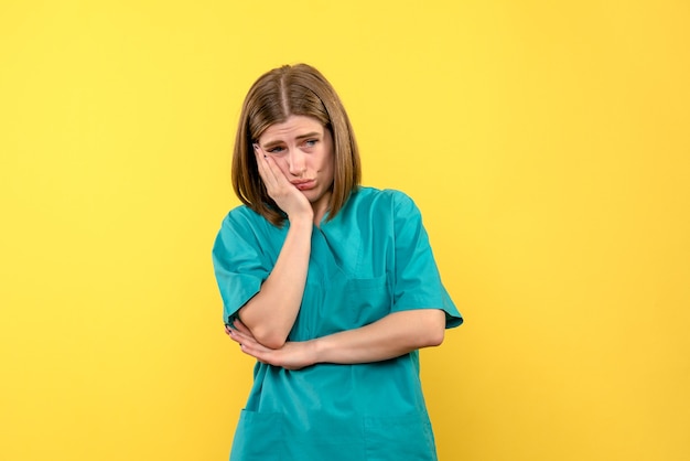 Vista frontal de uma médica com expressão estressada na parede amarela