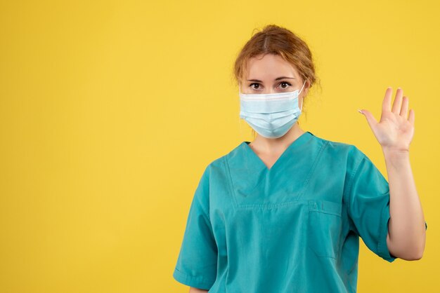 Vista frontal de uma médica com máscara protetora estéril na parede amarela