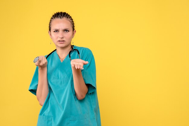 Vista frontal de uma médica em um traje médico confuso na parede amarela