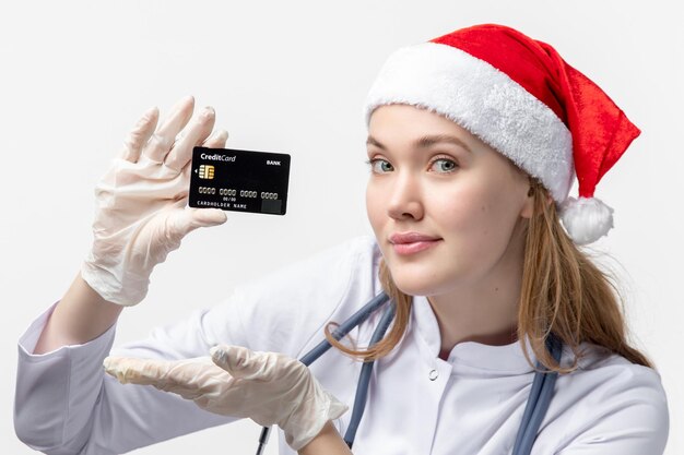 Vista frontal de uma médica segurando o cartão do banco na parede branca