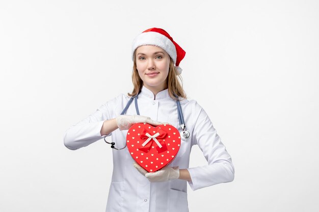 Vista frontal de uma médica segurando um presente de feriado na parede branca