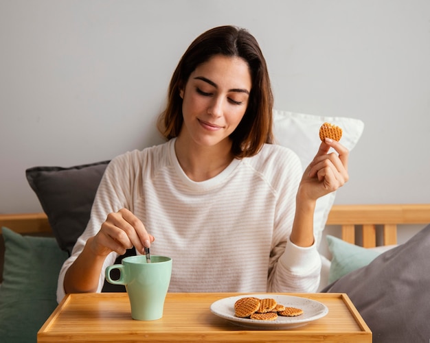 Vista frontal de uma mulher comendo e tomando café em casa