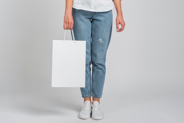 Vista frontal de uma mulher de jeans segurando uma sacola de compras