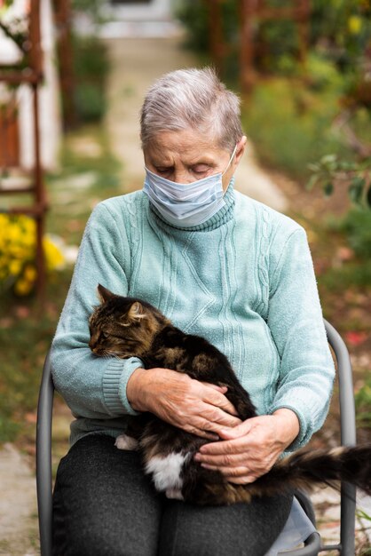 Vista frontal de uma mulher idosa com máscara médica e gato na casa de repouso
