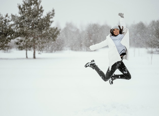 Vista frontal de uma mulher pulando no ar ao ar livre no inverno