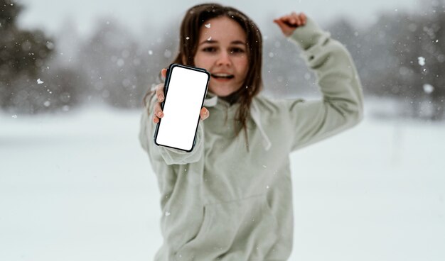 Vista frontal de uma mulher segurando um smartphone e pulando no ar ao ar livre no inverno