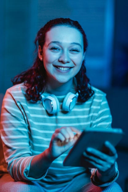 Vista frontal de uma mulher sorridente em casa usando fones de ouvido e tablet