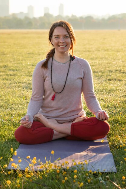 Vista frontal de uma mulher sorridente meditando ao ar livre no tapete de ioga