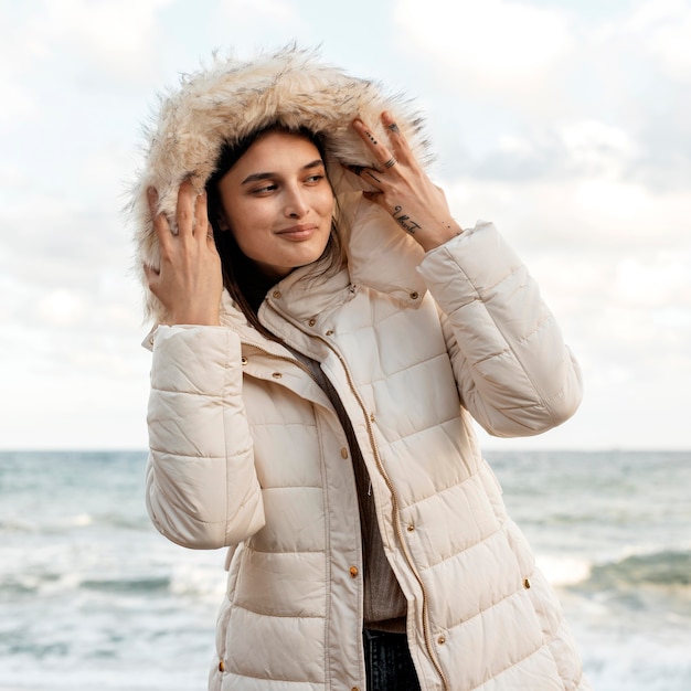 Foto grátis vista frontal de uma mulher sorridente na praia com jaqueta de inverno