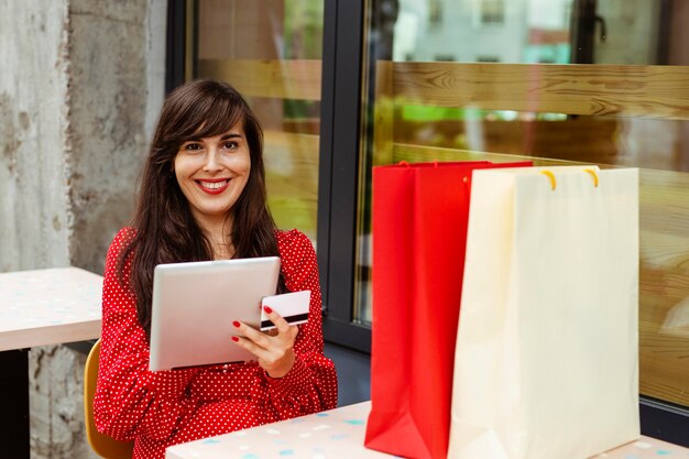 Vista frontal de uma mulher sorridente pedindo itens à venda usando tablet e cartão de crédito