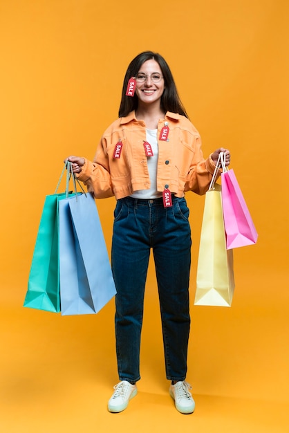 Vista frontal de uma mulher sorridente posando com sacolas de compras e etiquetas