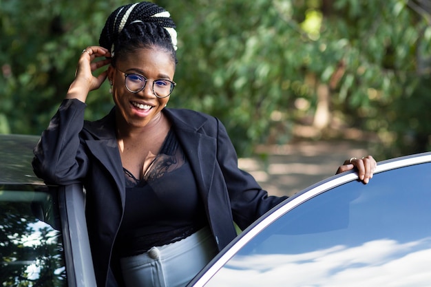 Vista frontal de uma mulher sorridente posando com seu carro novo