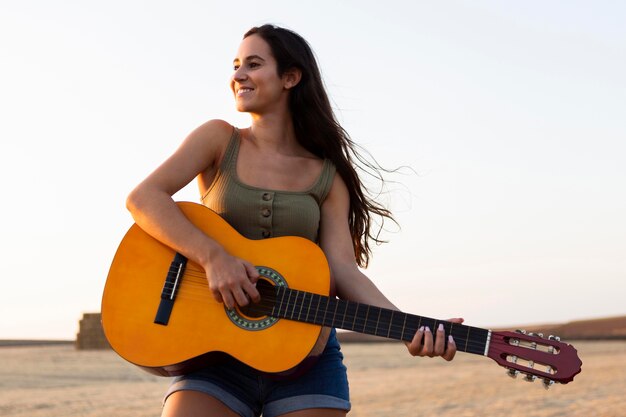 Vista frontal de uma mulher sorridente tocando violão na natureza