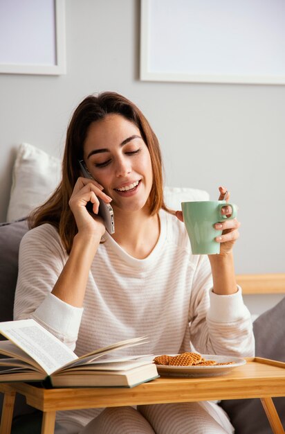 Vista frontal de uma mulher tomando café em casa e falando ao telefone em casa