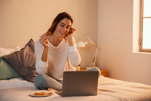 Vista frontal de uma mulher usando o laptop em casa e falando ao telefone