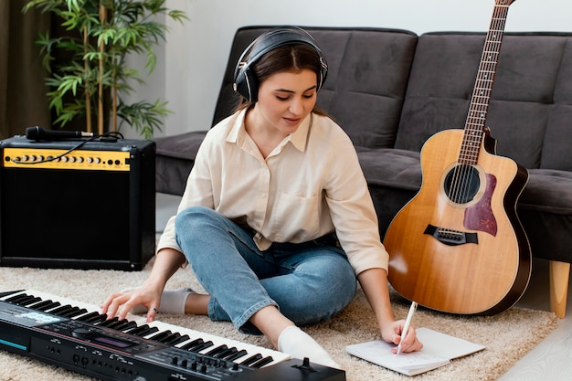 Vista frontal de uma musicista com teclado de piano e violão escrevendo músicas