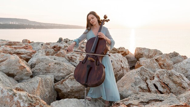 Vista frontal de uma musicista tocando violoncelo do lado de fora