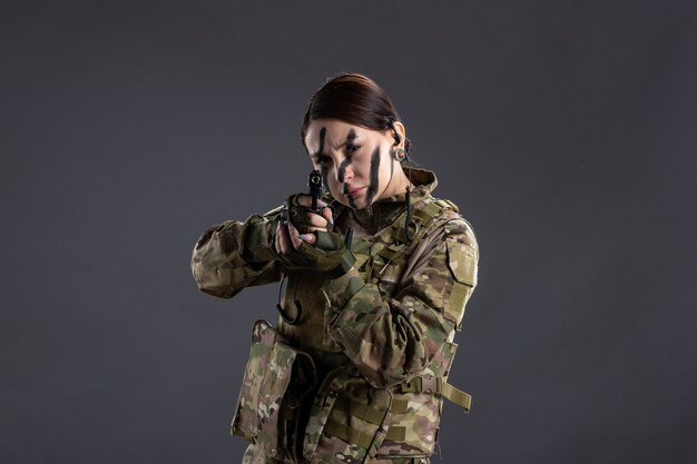 Vista frontal de uma soldado mirando a arma em uma parede escura de camuflagem